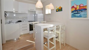 A modern kitchen with white cabinetry, a dining table, and two pendant lights. - Seaside Charm Apartment in Rovinj (Rovinj)