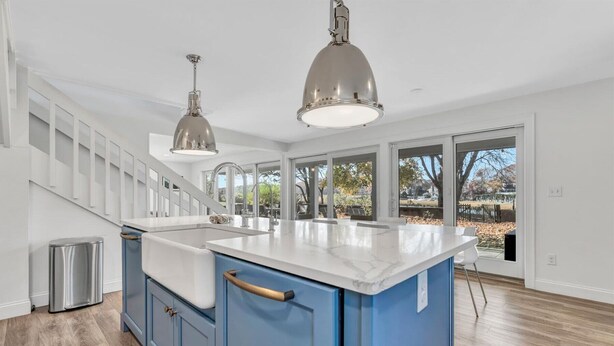 A kitchen with a large island, stainless steel sink, and blue cabinets. There are two pendant lights above the island. - Waterfront Retreat with Private Dock and Fire Pit  |  Sleeps 8, Outdoor Dining, Spa-Style Primary, Chef’s Kitchen w/ Dual Dishwashers, Gas Fireplace, River Views, Bright Open Layout, Central A/C, Perfect Coastal Escape for Families, 24 Hr Hospitality (Falmouth)