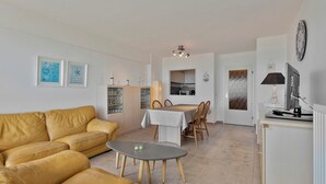 A modern living room with a sofa, a dining table, and chairs. There is a kitchen area visible in the background.
