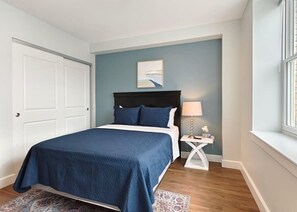 Un dormitorio con una cama, una mesita de noche, una lámpara y una ventana.