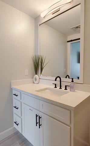 Un baño moderno con tocador blanco, un espejo grande y una planta.