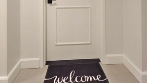 Una puerta blanca con un cartel que dice '406', un teclado numérico y un picaporte. Un felpudo con la palabra 'welcome' está adelante.