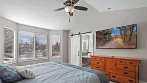 A bedroom with a bed, a dresser, a ceiling fan, and a wall-mounted TV displaying a mountain biking scene. - 10 Minutes to the Unitas! Full-Home Francis Rental (Kamas)