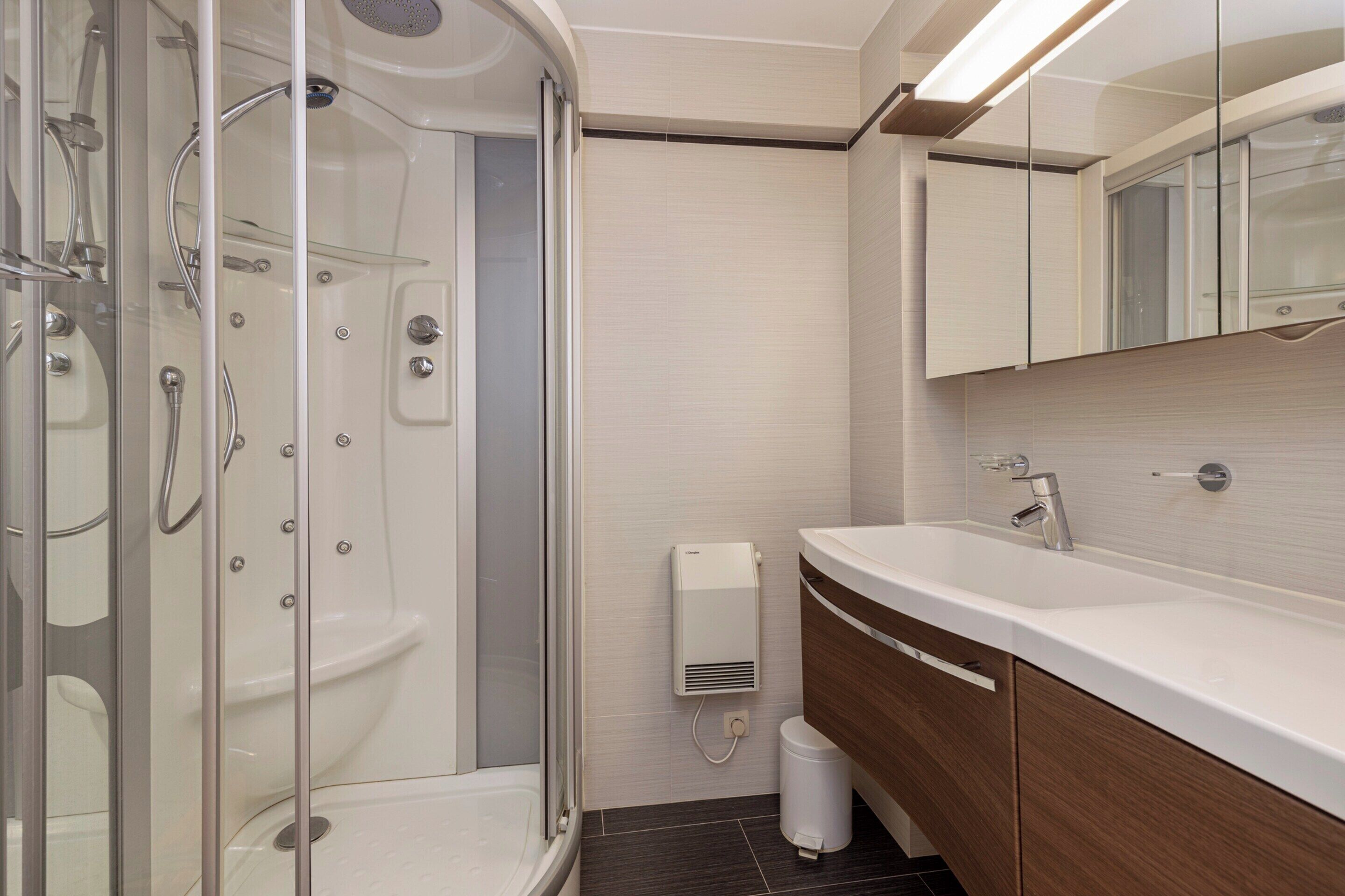 A modern bathroom with a glass-enclosed shower, a white sink, and a wooden vanity.