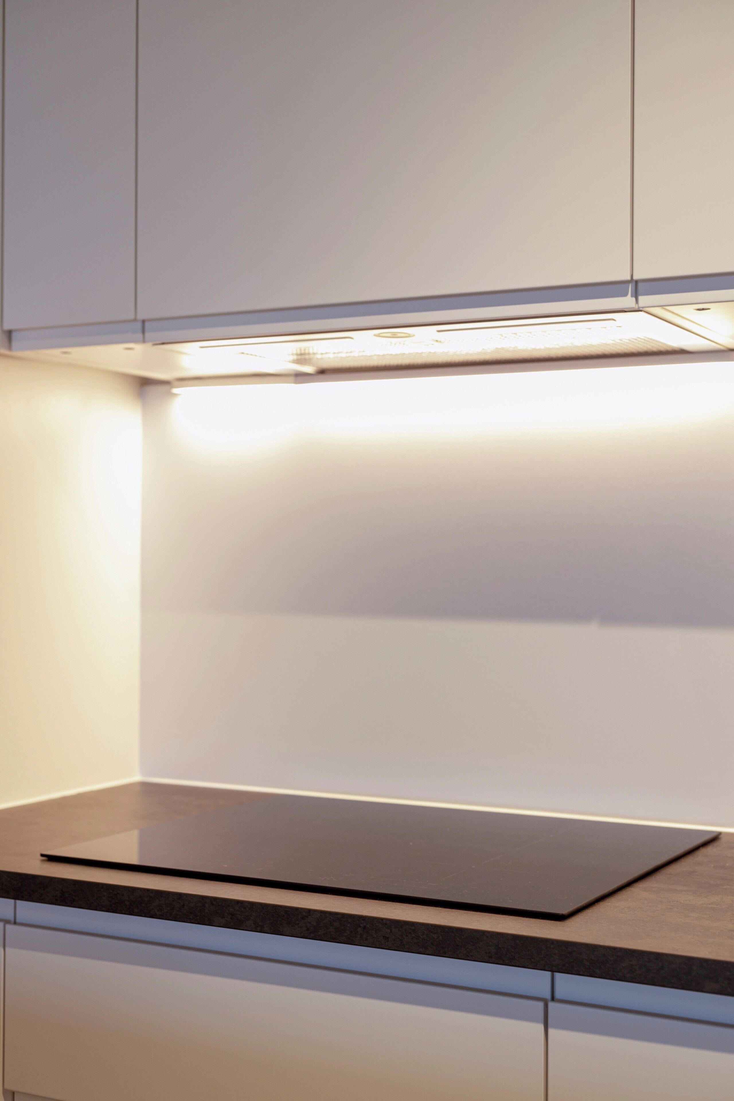 A kitchen with white cabinets, a black countertop, and under-cabinet lighting.