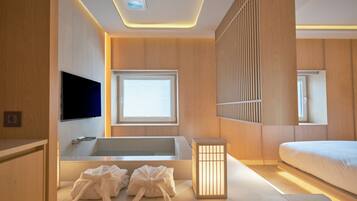 Un baño moderno con bañera, ducha e inodoro. Hay una ventana que proporciona luz natural y un televisor montado en la pared.