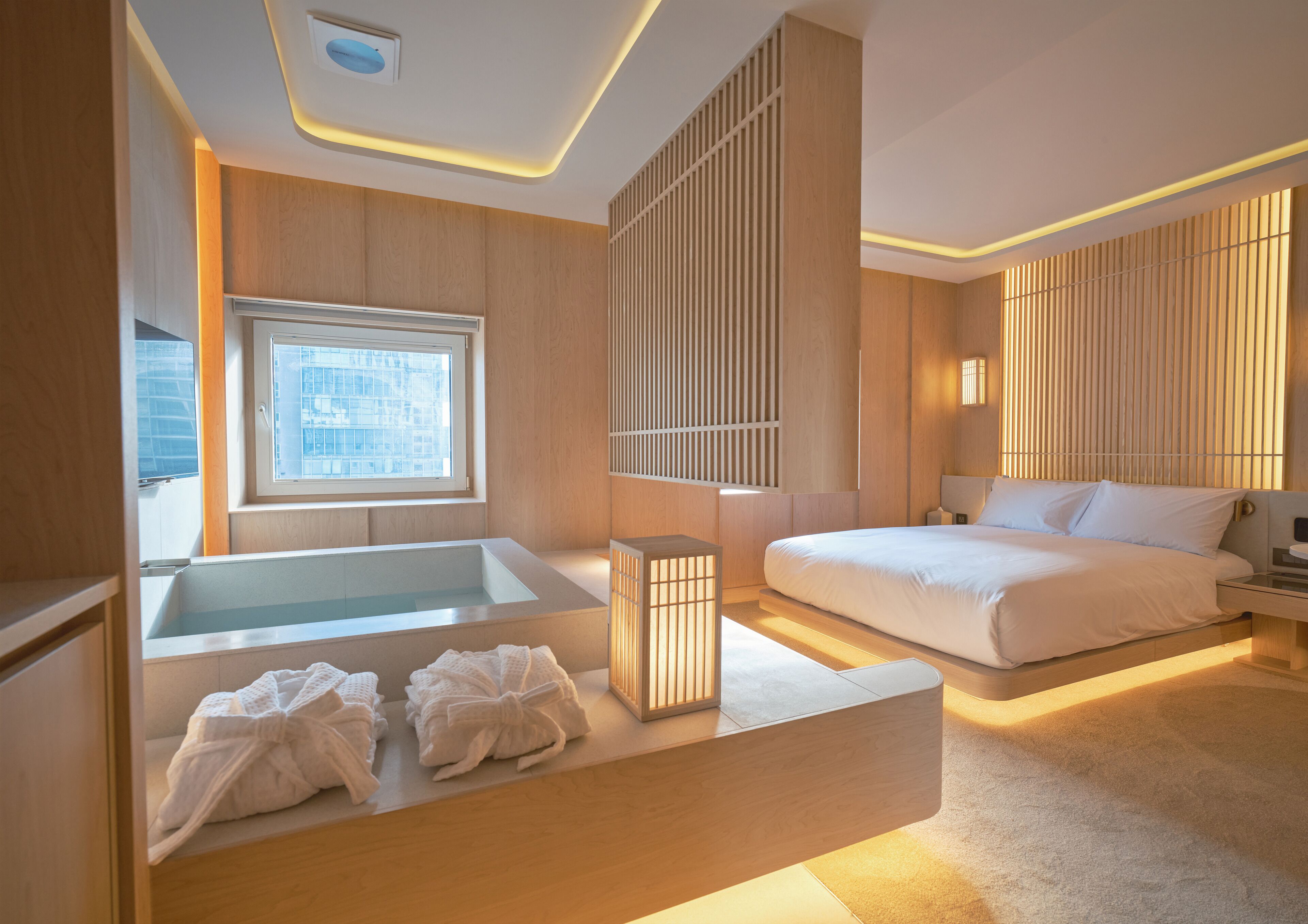 Quarto de hotel moderno com uma cama grande, uma banheira separada e uma janela com vista para a cidade.