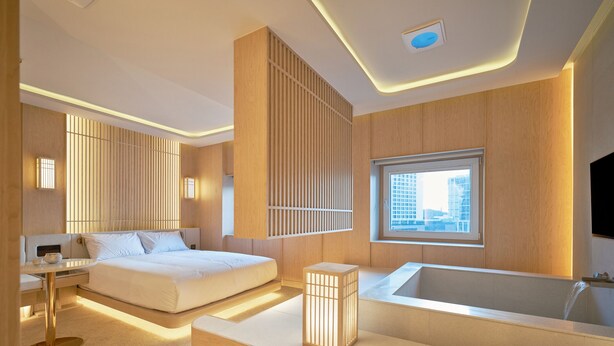 A modern hotel room with a large bed, a sitting area, a bathtub, and a city view through a window. - UH Continental CenterPoint (Busan)