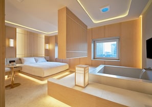 A modern hotel room with a large bed, a sitting area, a bathtub, and a city view through a window. - UH Continental CenterPoint (Busan)