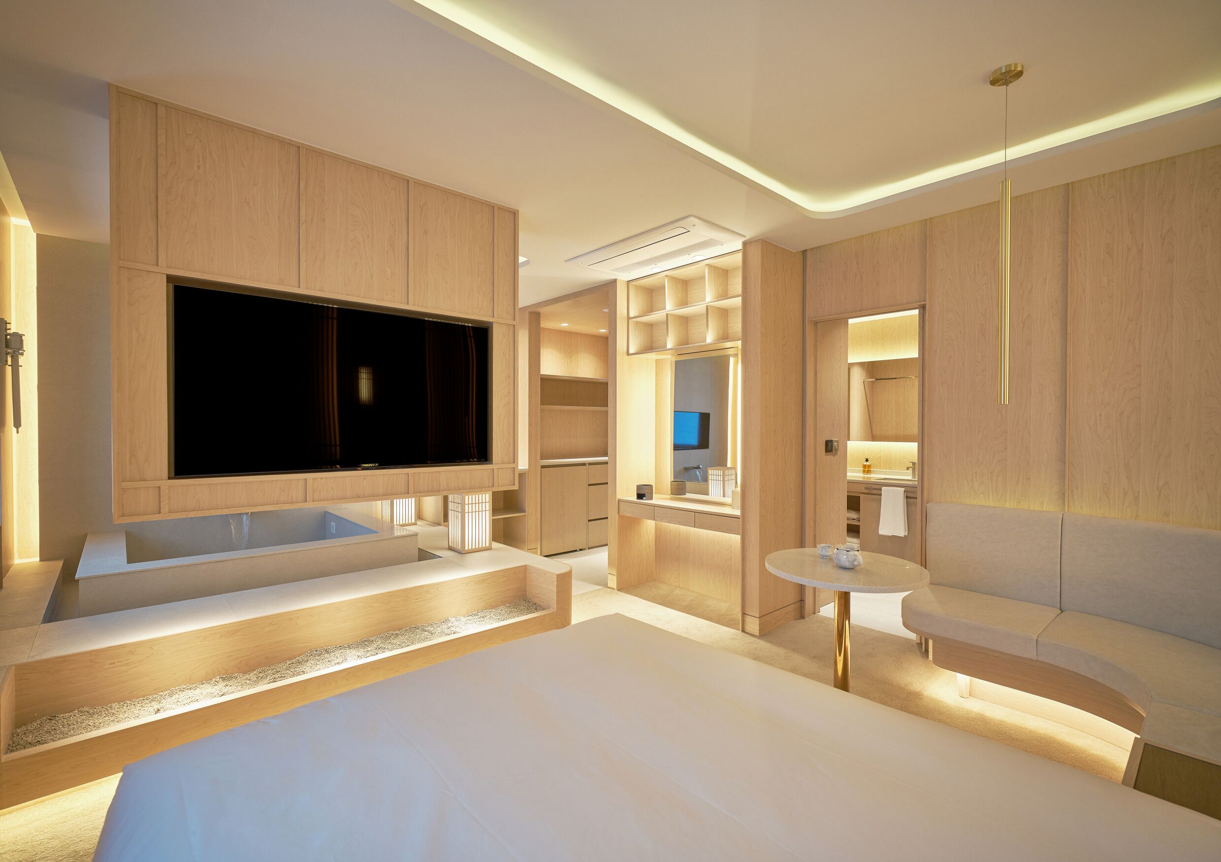 Una habitación de hotel moderna con una cama grande, televisión, bañera, una mesita y un espejo.