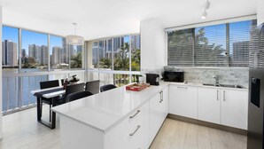Cocina moderna con una isla grande, armarios blancos y vistas de la silueta urbana a través de amplias ventanas.