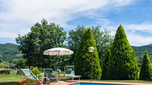 Una piscina con sillas de descanso y una sombrilla, rodeada de vegetación y árboles.