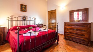 Un dormitorio con estructura de cama metálica, cómoda de madera, puerta de madera y un cuadro colgado en la pared.
