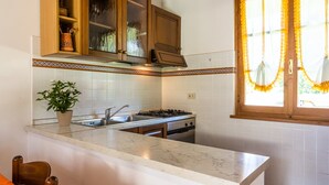 Una cocina con azulejos blancos, estufa, fregadero, armarios de madera y una ventana con cortinas.