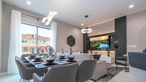 A modern dining area with a glass table, grey chairs, and a TV mounted on the wall. - Luxury 3BR home with Mario Bros Room Near Disney (Kissimmee)