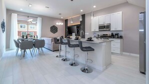 A modern kitchen with a central island, bar stools, and a dining area with a table and chairs. - Luxury 3BR home with Mario Bros Room Near Disney (Kissimmee)