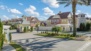 A residential street with houses, a gated entrance, and a clear sky.