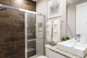 A modern bathroom with a glass shower enclosure, a white sink, and a framed artwork on the wall.