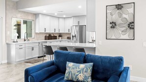 Una cocina moderna con armarios blancos, un refrigerador de acero inoxidable y una zona de comedor con taburetes de bar.