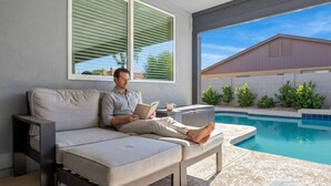 Una persona descansando en un sofá junto a una piscina, con vista a una casa y vegetación.