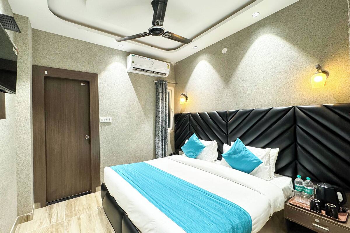 A hotel room with a bed, a ceiling fan, an air conditioning unit, a nightstand with a tray, and a door.
