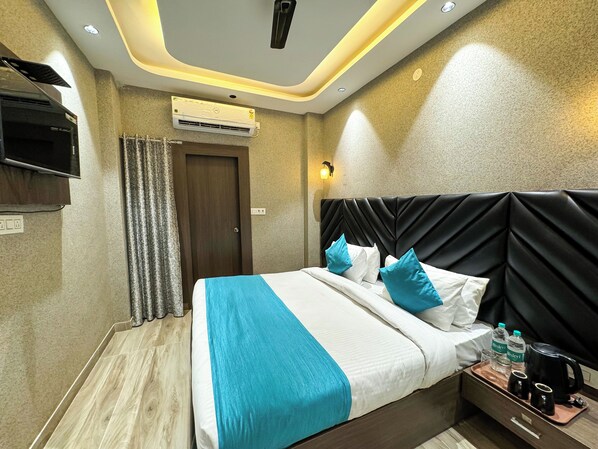 A hotel room with a bed, a TV, an air conditioner, a nightstand with a coffee maker, and a wall-mounted light. - Wanna stay haridwar (Haridwar)