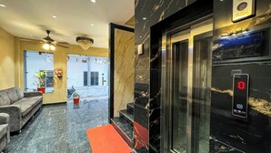 A modern lobby with a marble floor, a sofa, a red mat, a chandelier, and an elevator. - Wanna stay haridwar  (Haridwar)