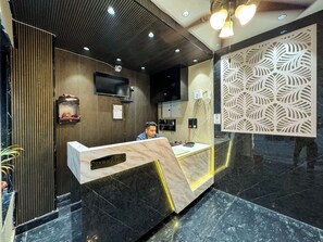 A reception desk with a marble top, a wooden panel wall, a decorative leaf-patterned panel, and a mounted television. - Wanna stay haridwar  (Haridwar)
