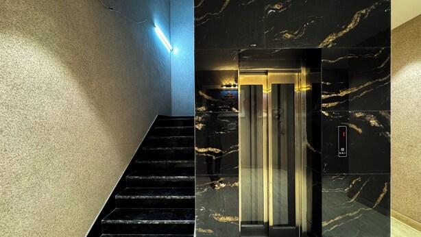A modern elevator with a sleek black and gold marble finish, a staircase with black steps, and a textured beige wall. - Wanna stay haridwar  (Haridwar)