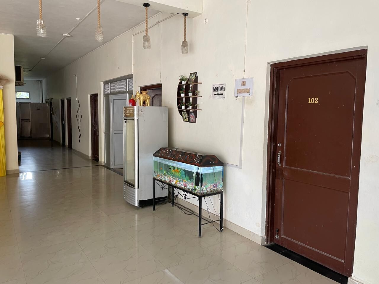 A hallway with a fish tank on a stand, a refrigerator, and a door labeled "102".
