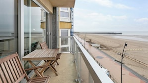 A balcony with a wooden table and chairs, overlooking a beach and a pier. - Apartment in Blankenberge by the Beach (Blankenberge)