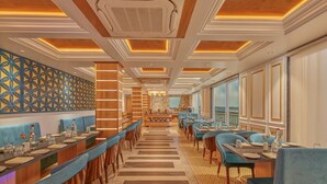 Een lange eetruimte met een centraal buffet, blauwe gestoffeerde zitplaatsen en een behang met patroon.
