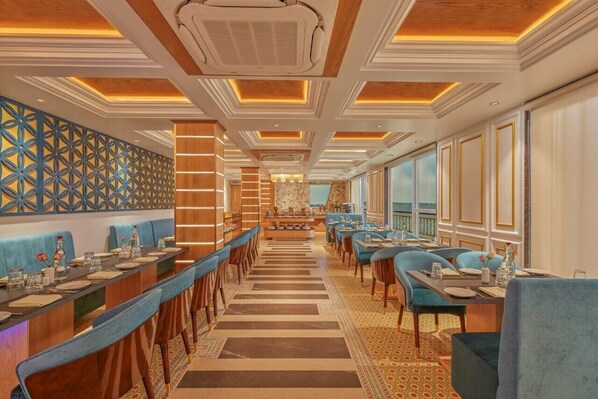 A long dining area with a central buffet, blue upholstered seating, and a patterned wall.