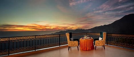 A balcony with two chairs and a table, overlooking a scenic sunset view.
