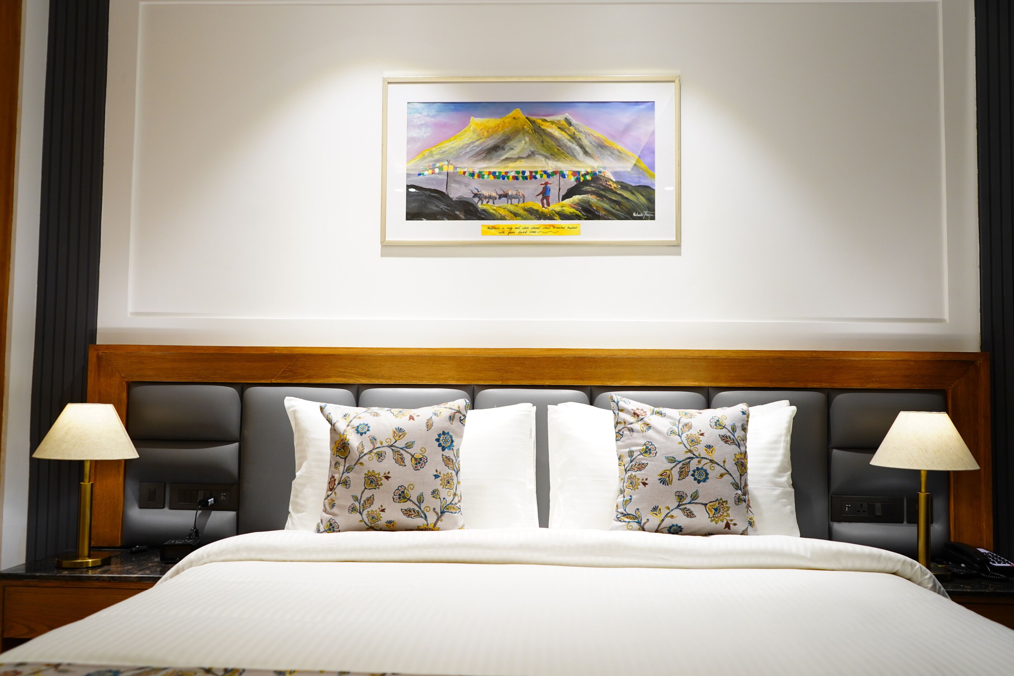 A hotel room with a large bed, two nightstands, a framed picture on the wall, and a wooden headboard.