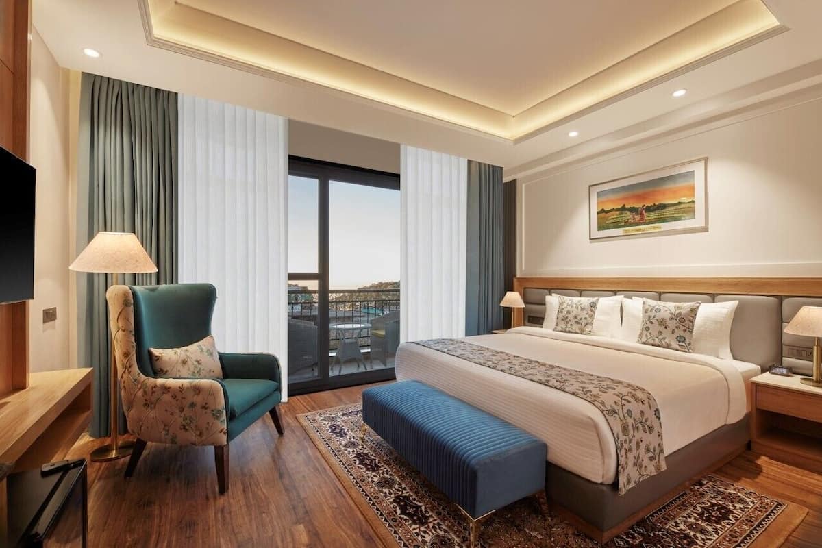 Een moderne hotelkamer met een groot bed, een zithoek met een stoel, een televisie en een schilderij aan de muur.