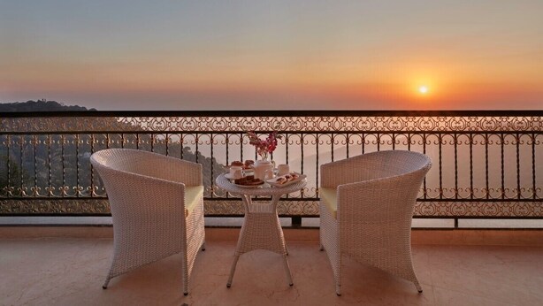 Een balkon met rieten meubels en een gedekte tafel voor thee, met uitzicht op een zonsondergang.