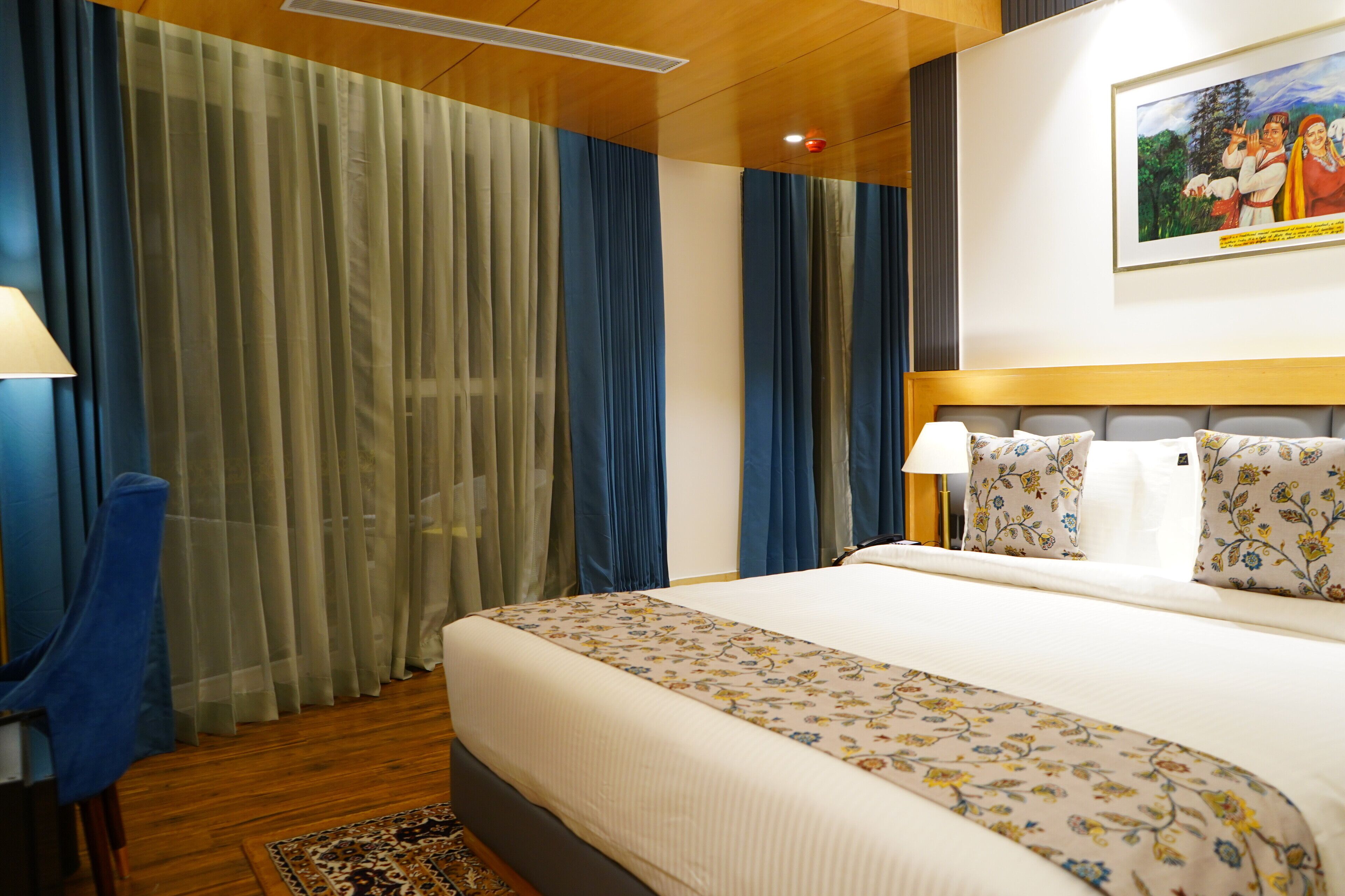A hotel room with a large bed, a headboard, a nightstand, a lamp, and a painting on the wall.