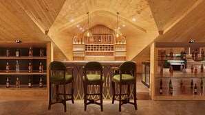 Een houten interieur met een bar, inclusief flessenkasten vol drank, en een zithoek met groene fauteuils.