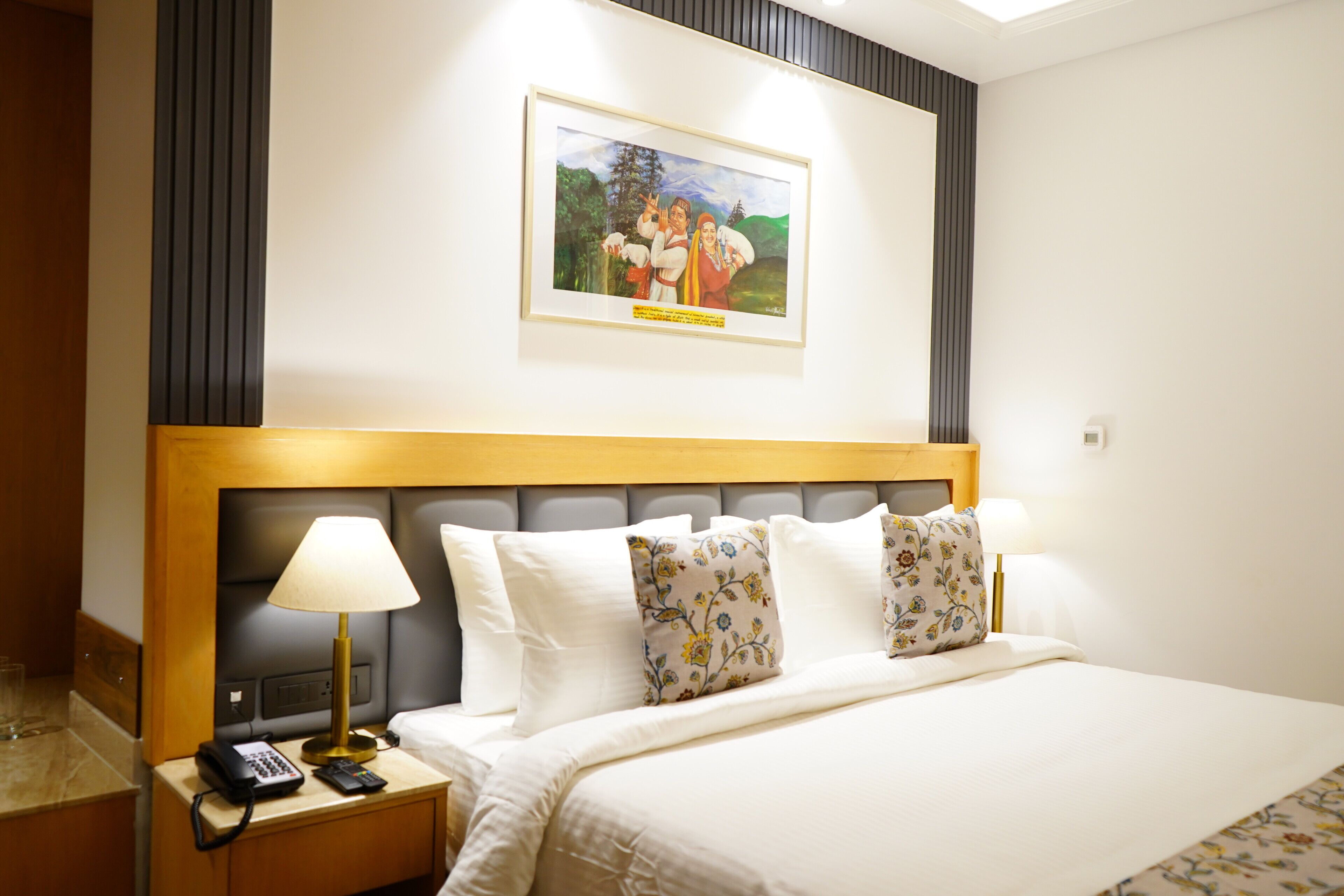 A hotel room with a bed, bedside lamps, a phone, and a framed picture on the wall.