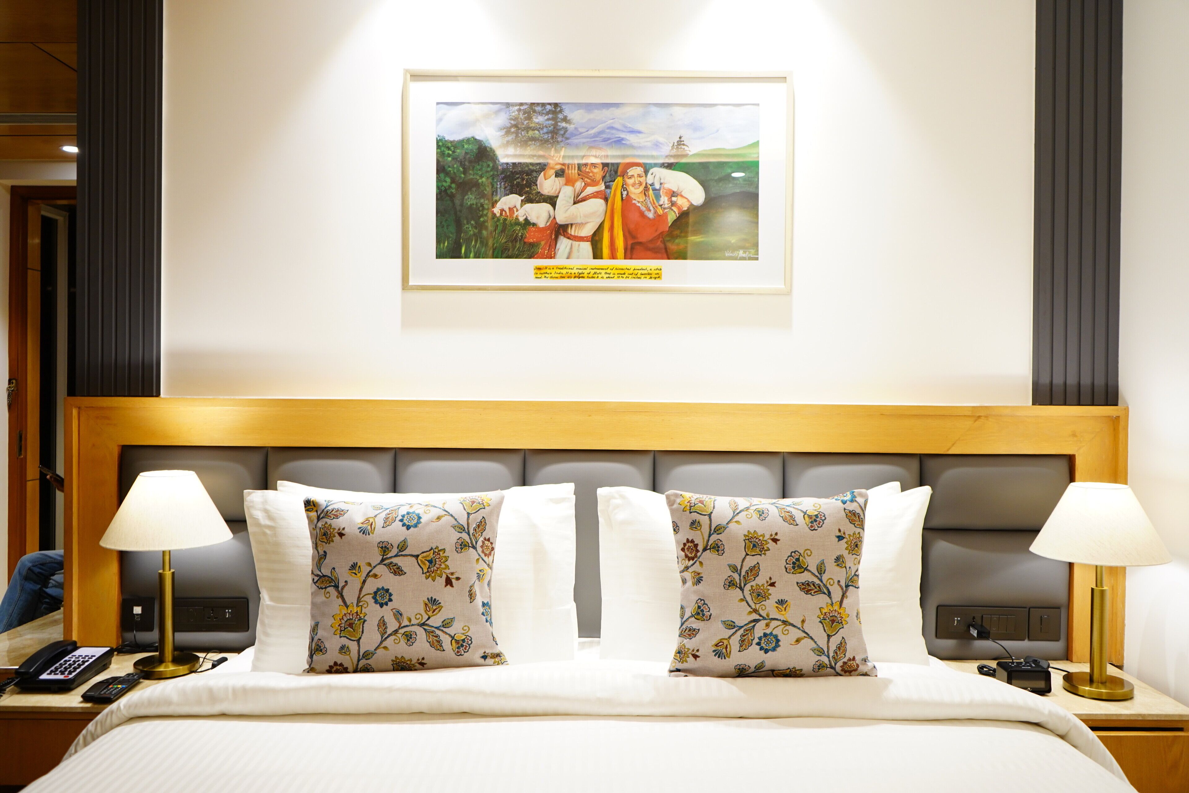 Une chambre d’hôtel avec un grand lit, deux lampes de chevet, un tableau encadré au mur et une tête de lit en bois.
