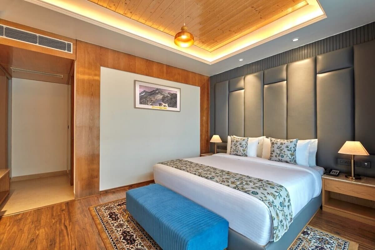 Een moderne hotelkamer met een groot bed, houten lambrisering, een ingelijst schilderij aan de muur en een bankje bij het bed.