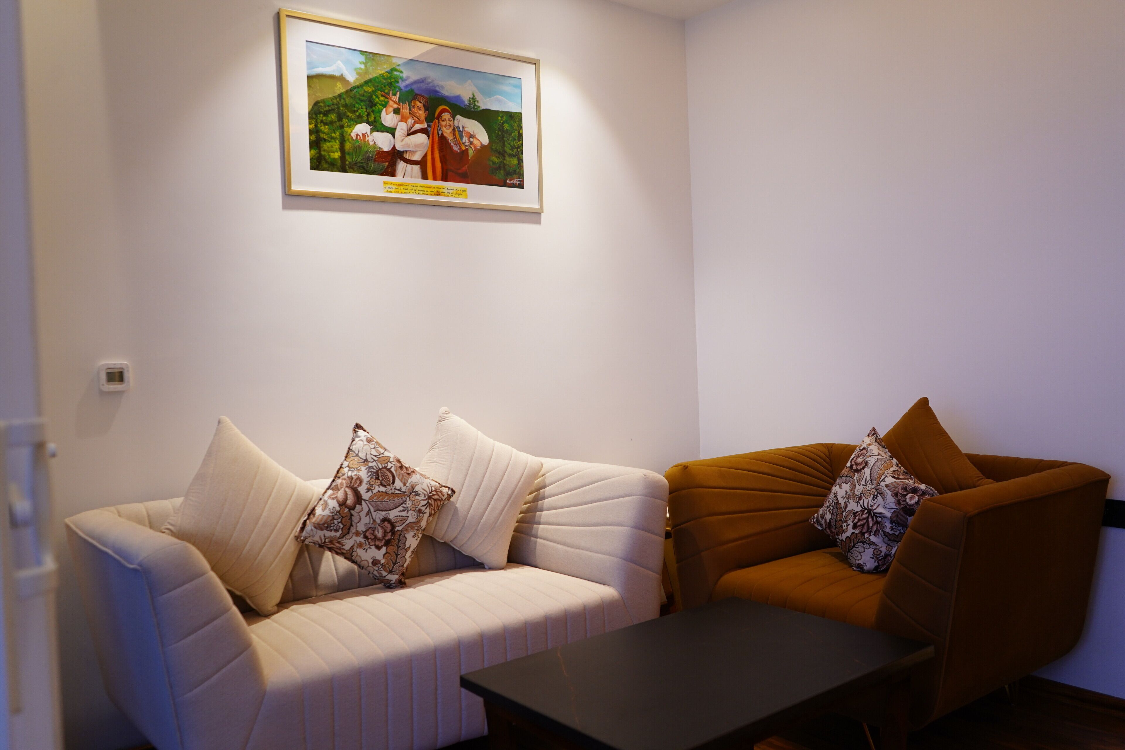 A living room with a sofa and armchair, a framed painting on the wall, and a small table.
