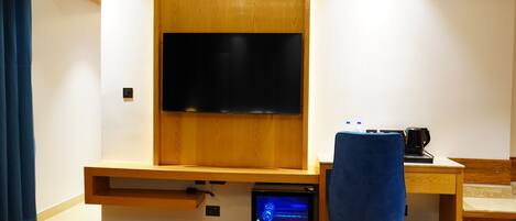 A modern room with a wooden desk, a blue chair, a television mounted on the wall, and a small computer on the desk.