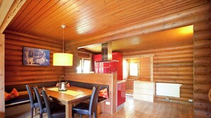 L’intérieur d’une cabane en rondins comprend un coin repas, des murs en bois, une cuisine rouge et une cheminée.
