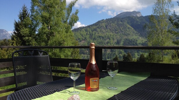 Une table avec une bouteille de Martini, deux verres et deux pierres, le tout posé sur un tapis vert, avec une chaîne de montagnes en arrière-plan.