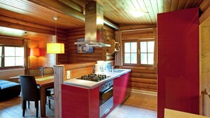 L’intérieur d’une cabane en rondins, avec un îlot de cuisine, une table à manger, des chaises et une cheminée.
