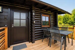 Una baita di legno con un patio in legno, un tavolo da pranzo con sedie e il numero '6' appeso al muro.