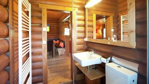 Une salle de bain rustique, aménagée dans une cabane en rondins, avec un lavabo, un miroir et des toilettes en bois.
