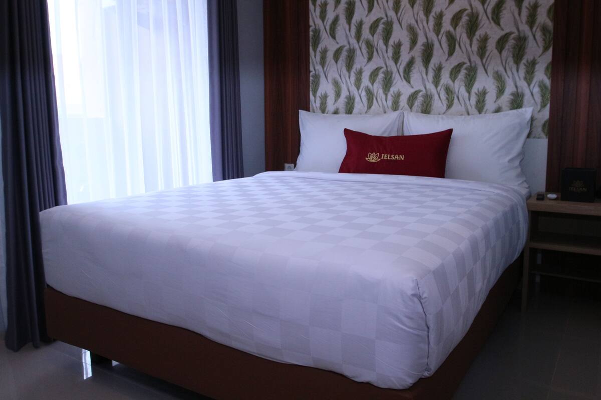 Habitación de hotel con una cama grande, una mesita de noche y una pared con estampado de hojas.